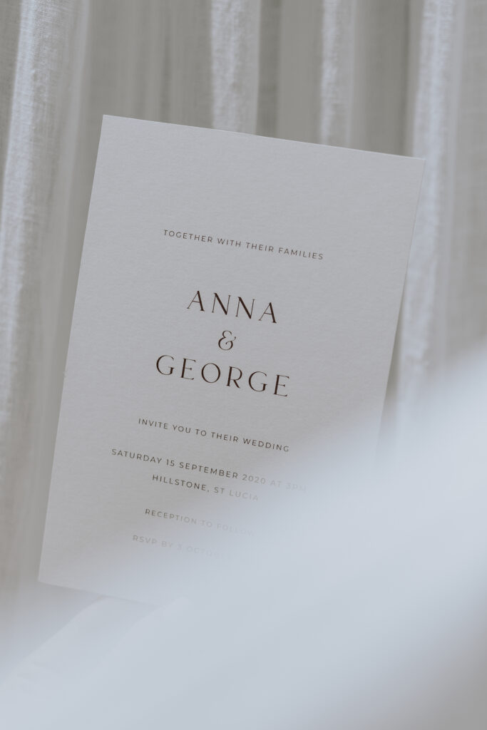 Photo of a white wedding invitation with brown writing shot in front of a white curtain