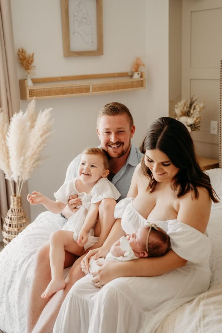 Rebel with her husband and two little girls sitting on a bed.