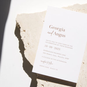 White wedding invitation with brown text placed on top of a broken piece of travertine stone.