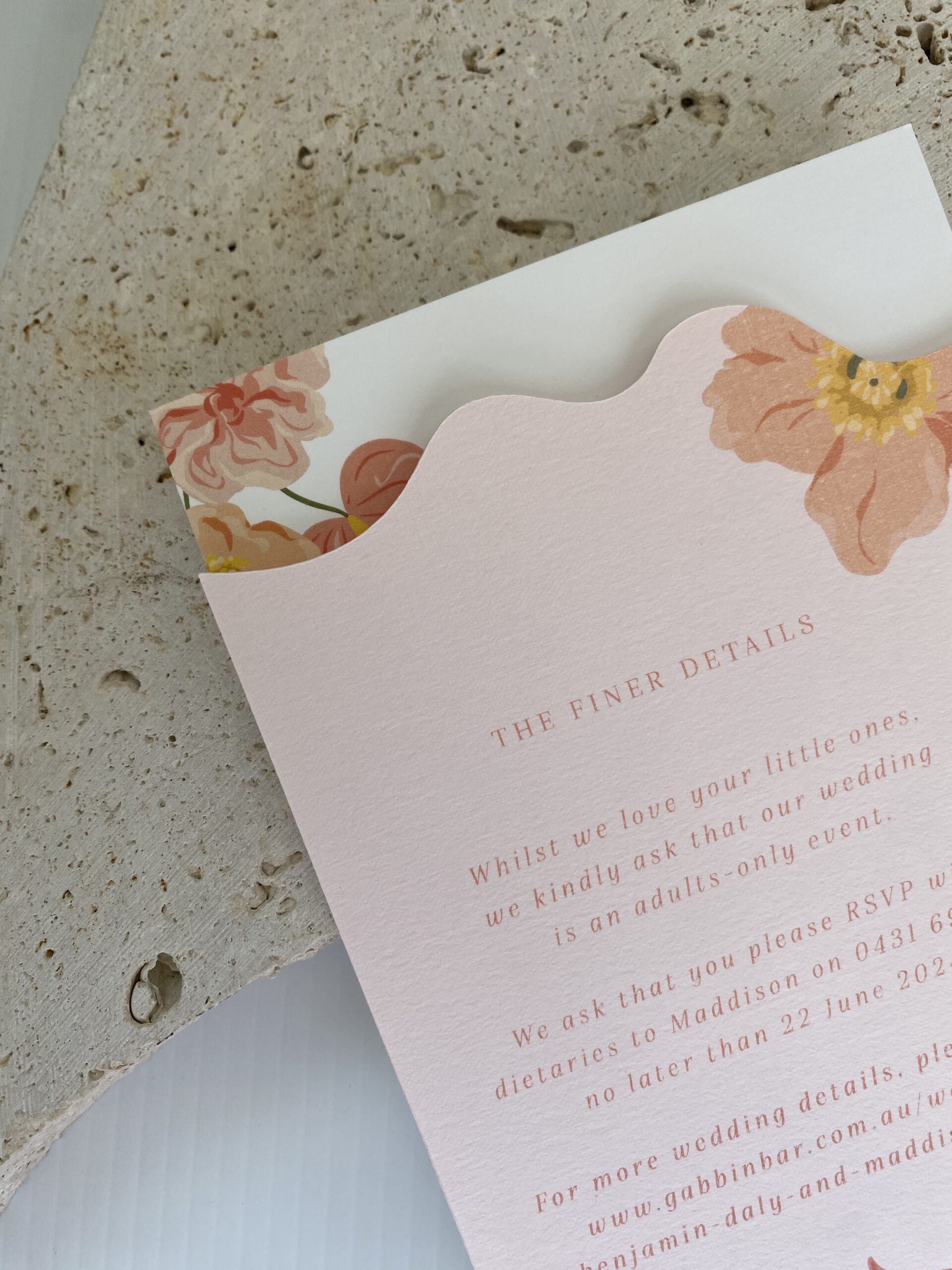 Pink and white layered invitation suite placed on top of a decorative stone.