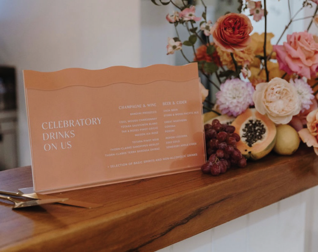 Orange wedding sign placed on a bar next to an arrangement of orange and pink florals.