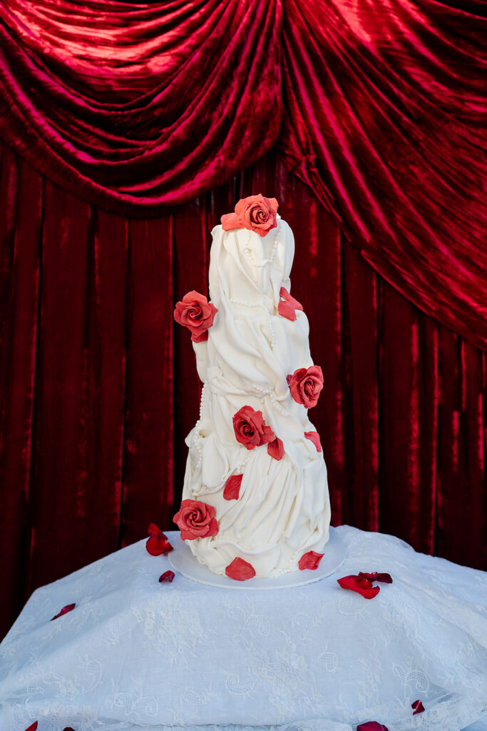 White wedding cake sitting in front of a red satin backdrop.