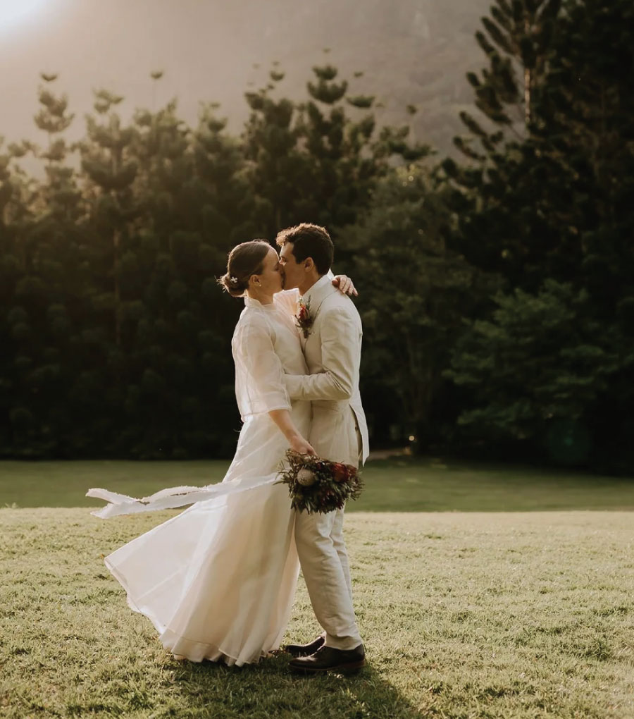 Bride and Groom kissing on grass with trees behind them